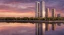 The image depicts a city skyline at sunset, with a tall, modern building featuring a curved design and two towers dominating the center. The building is reflected in the calm waters below, creating a mirror-like effect. The sky is a mix of pink, orange, and purple hues, providing a beautiful backdrop to the scene. The