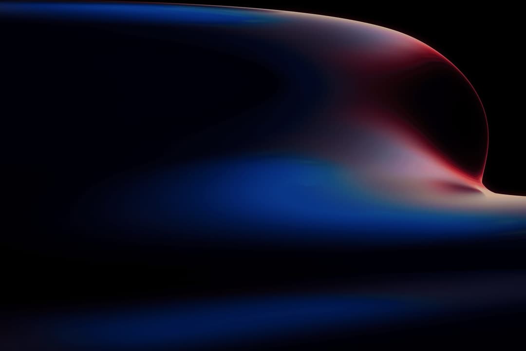 The image presents a digital art piece featuring a gradient of colors, primarily blue and red, against a black background. The colors blend and flow into each other, creating a sense of movement and fluidity. The blue color is concentrated in the center, transitioning into red towards the right side of the image. The r