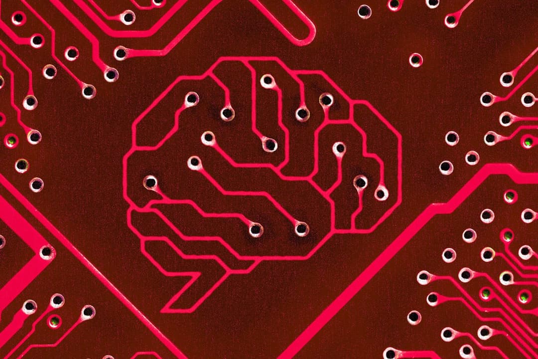 The image shows a close-up view of a circuit board, primarily dark red or maroon in color, with a pattern of small white dots and lines. The circuit board features a prominent pink outline of a human brain, composed of interconnected lines and dots. The brain outline is not a perfect representation of a human brain, bu
