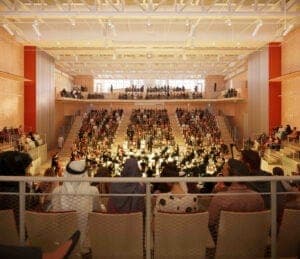 An interior view of a warmly lit hall with tiered seating, a crowd of spectators on the balconies, and a stage or orchestra in the center. No legible text is visible.
