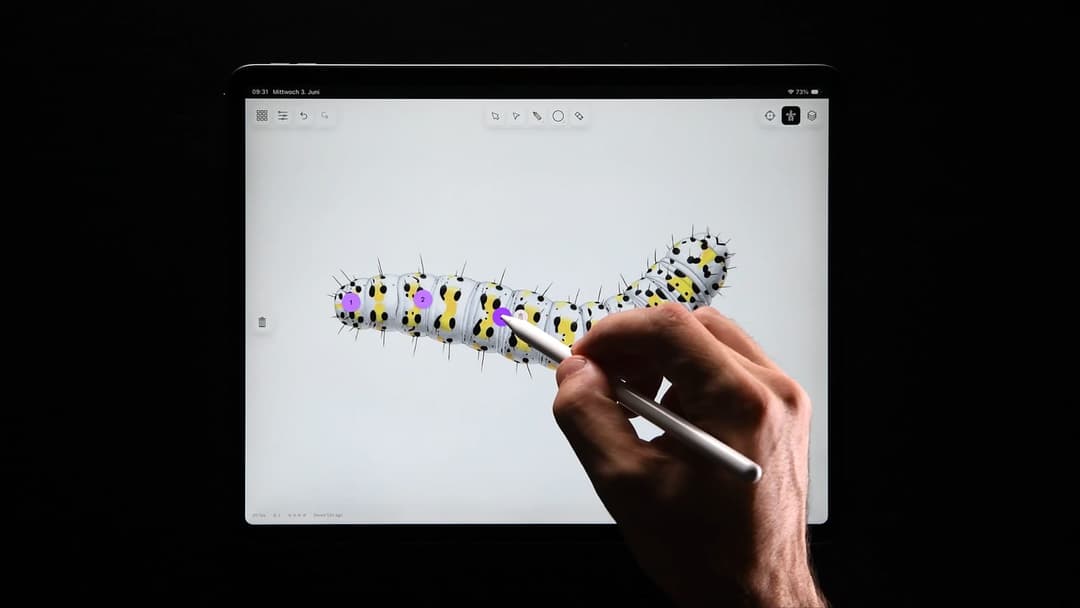 The image shows a person's hand holding a white stylus, poised over a tablet screen displaying a 3D rendering of a caterpillar. The caterpillar is primarily white with black and yellow markings, and it is positioned in the center of the screen. The tablet screen is open to a drawing application, with a white background