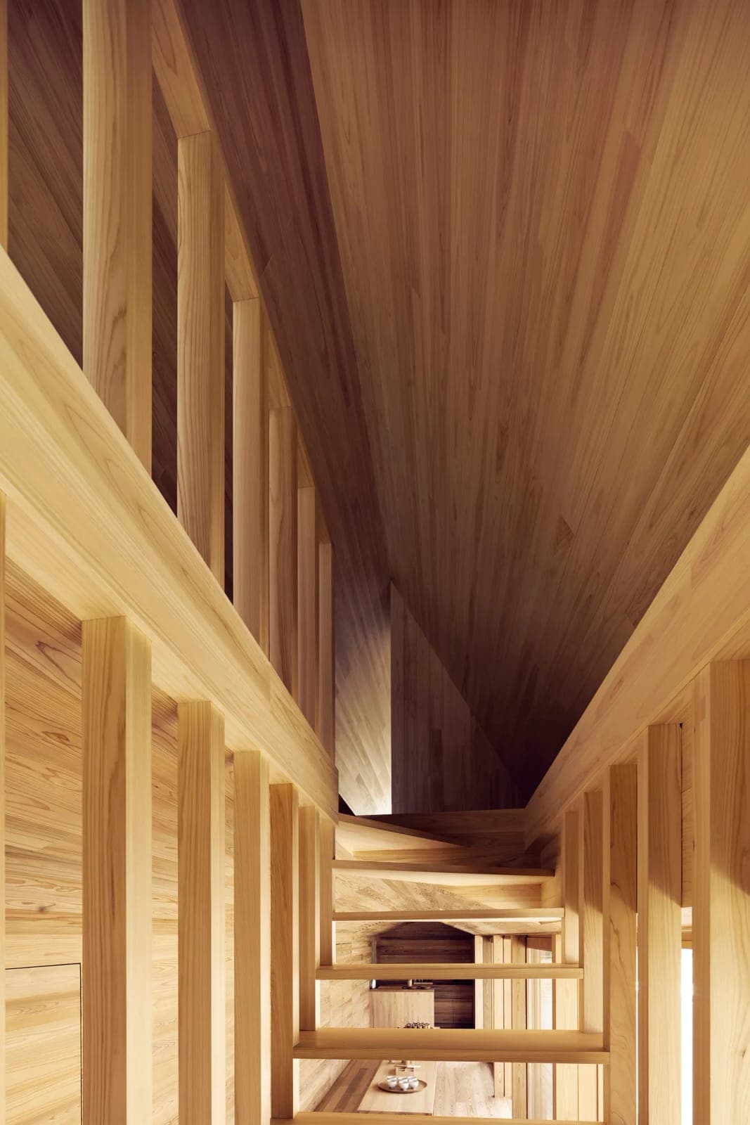 The image depicts a serene interior space with a wooden staircase ascending towards the ceiling. The staircase is constructed from light-colored wood and features a railing on the left side. The walls are also made of light-colored wood, and the ceiling is composed of wooden planks. The perspective of the image is from