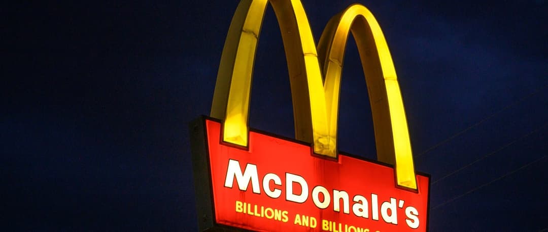 The image shows a McDonald's restaurant sign against a dark blue sky. The sign is illuminated by a bright yellow arch, which is the iconic symbol of the fast-food chain. The sign is primarily red with white lettering, and it displays the text "McDonald's" and "Billions and Billions" in white. The sign is positioned in