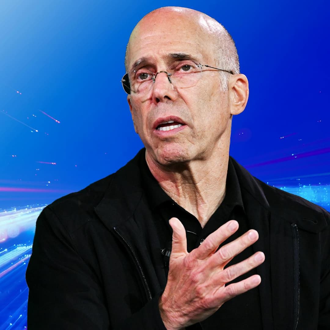 The image shows a man with a bald head and glasses, wearing a black jacket over a black shirt. He is standing against a vibrant blue background with streaks of light, possibly suggesting a futuristic or technological setting. His right hand is raised to his chest, and his left hand is slightly open, as if gesturing whi