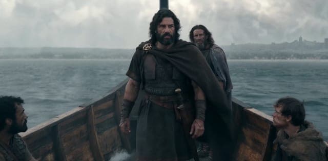 The image shows a group of four men aboard a wooden boat on a stormy sea. The boat is positioned in the center of the frame, with the men standing on either side. The man in the foreground is wearing a dark brown or black cloak and a brown or dark-colored tunic, and he is holding a sword in his right hand. The other th
