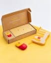 The image shows a cardboard box with a yellow and red design, open on a yellow background. The box contains a set of yellow cards with a red McDonald's logo and a matching red and yellow mouse. A yellow and red pouch with a yellow and red design is also visible, likely containing additional McDonald's themed items. The