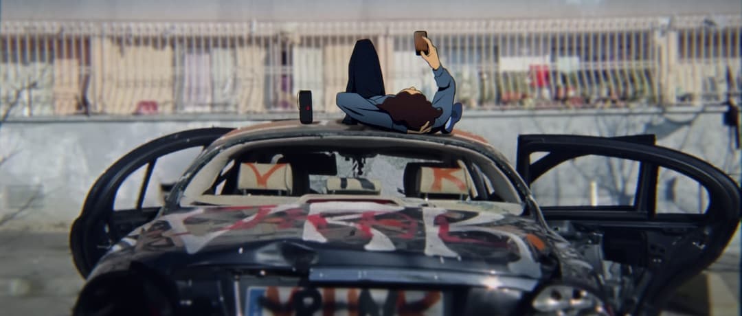 The image shows a person lying on their back on the hood of a damaged car. The car's hood is covered in graffiti, and the car's doors are open. The person is wearing a blue shirt and dark pants, and is holding a phone in their right hand. The car appears to be in a state of disrepair, with visible damage to the front a