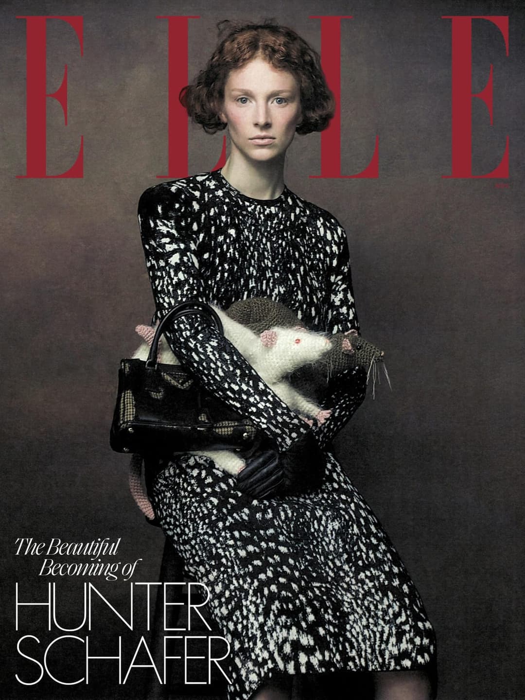 The image is a magazine cover featuring a woman with curly hair and a black and white patterned dress. She is holding a small, white rat in her arms. The woman is wearing black gloves and holding a black purse. The background is a dark gray or brown color. The magazine title "ELLE" is displayed in large, red letters at