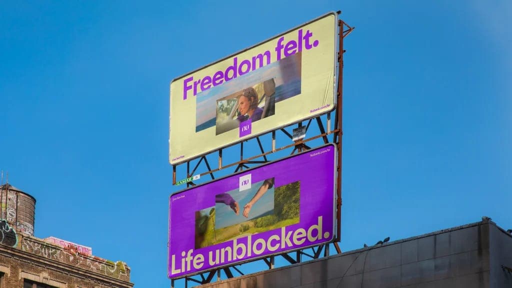Two Nu billboards stand against a blue sky, one reading 'Freedom felt.' and the other 'Life unblocked.', both with the Nu logo and 'nubank.com/nu'.