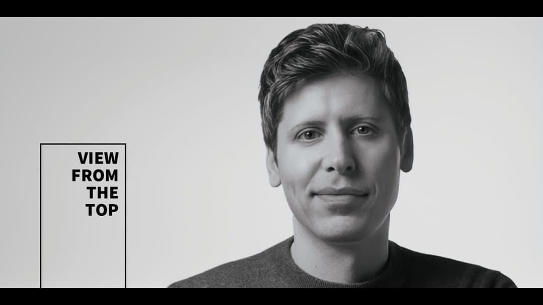 The image is a black and white portrait of a man with short, dark hair. He is wearing a dark-colored, possibly gray or dark blue, shirt. The man's gaze is directed towards the camera, and he has a slight smile on his face. The background is a plain, light gray color. In the top left corner of the image, there is a blac