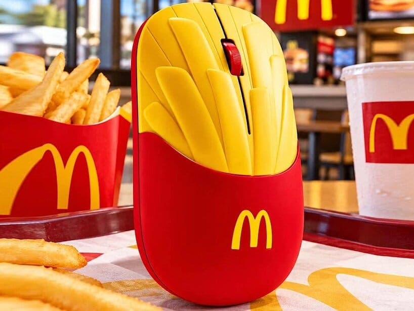 A McDonald's fries-shaped mouse stands upright on a restaurant tray beside a carton of fries and a drink cup. The golden arches logo appears on the mouse, cup and fry carton, and the background shows a restaurant interior.