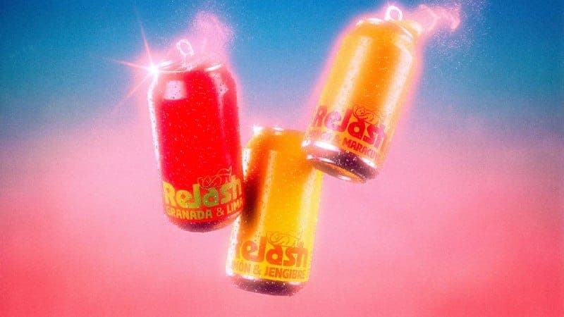The image shows three cans of Relash brand beverages, each with a different flavor: Granada & Lima, Mango & Mararcu, and Mon & Jengibre. The cans are suspended in mid-air against a gradient background that transitions from blue at the top to pink at the bottom. The cans are slightly tilted, giving a dynamic impression.