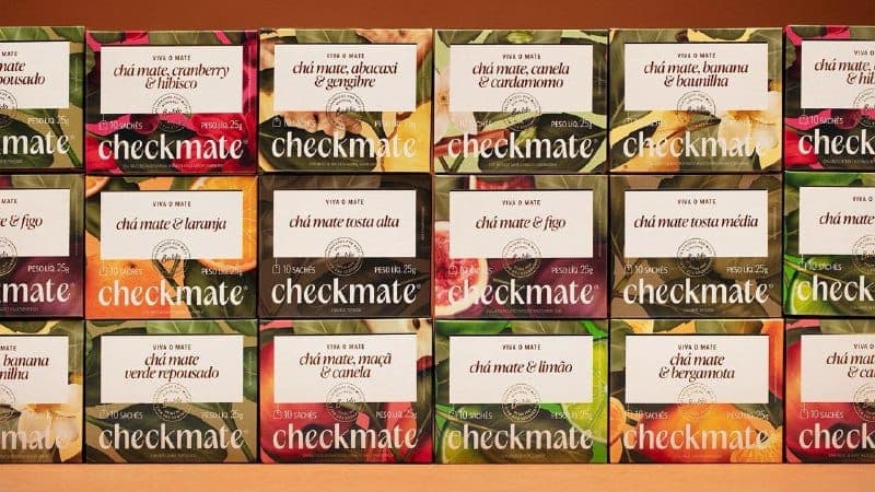 The image presents a neatly arranged collection of checkmate tea boxes, each adorned with a vibrant floral design and the brand name "checkmate" prominently displayed in white. The boxes are arranged in a grid pattern, with three rows and four columns, creating a visually appealing display. Each box features a differen