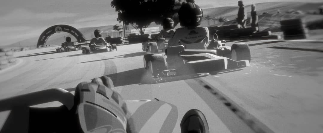 This black and white image captures a moment from a racing video game, likely a first-person perspective. The main focus is on a go-kart track, with a blurred background that suggests a race or competition. The track is marked with a large archway in the background, and several go-karts are visible, with at least one i