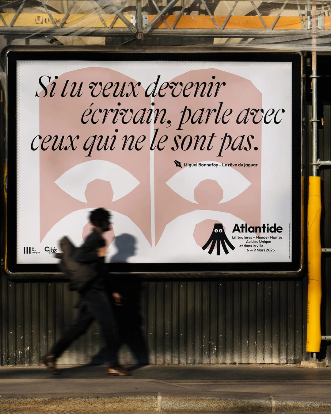 The image shows a large billboard on a metal structure, likely part of a construction site or urban area. The billboard is primarily white with a pink/peach colored design featuring a stylized image of a person, possibly a nurse or doctor, and the text "Sí tu veux devenir écrivain, parle avec ceux qui ne le sont pas."