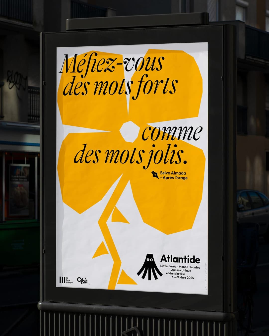 The image shows a vibrant poster for the "Atlantide" event, which took place from March 9th to March 9th, 2025, in Marseille, France. The poster is predominantly white with a striking yellow flower design at the center. The text on the poster is in French and reads "Méfiz-vous des mots forts comme des mots jolis." The