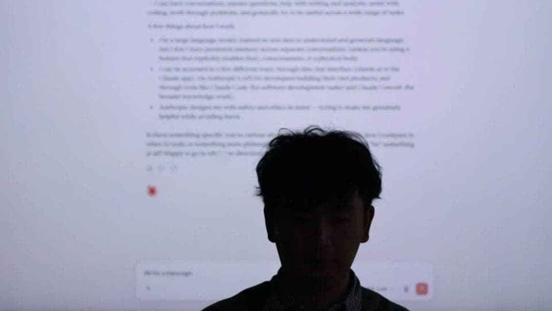The image shows a person standing in front of a computer screen displaying text. The person's face is partially obscured by the screen, and they appear to be wearing a dark-colored shirt. The computer screen is the central focus of the image, with the person standing in front of it. The text on the screen is in English