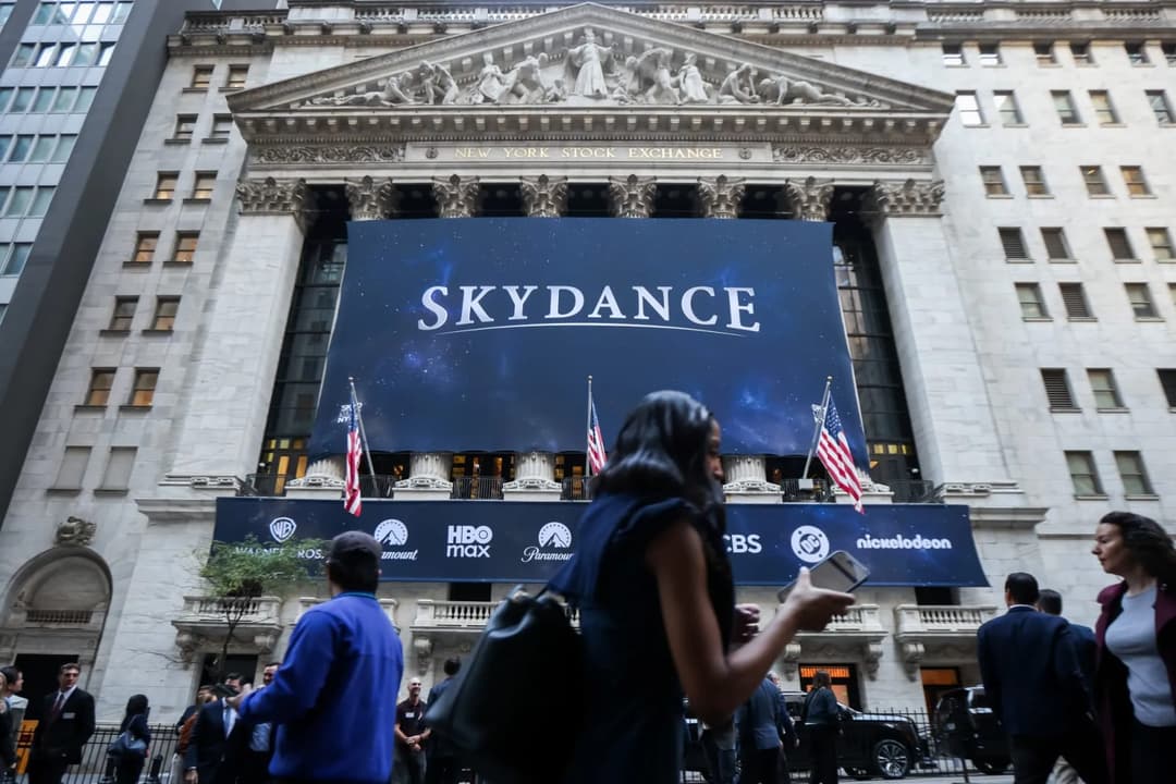 The image captures the grandeur of the New York Stock Exchange building, a neoclassical architectural marvel with a white facade and a dark blue roof. The building is adorned with a large banner displaying the words "SKYDANCE" in white letters against a dark blue background, and features several flags, including the Am