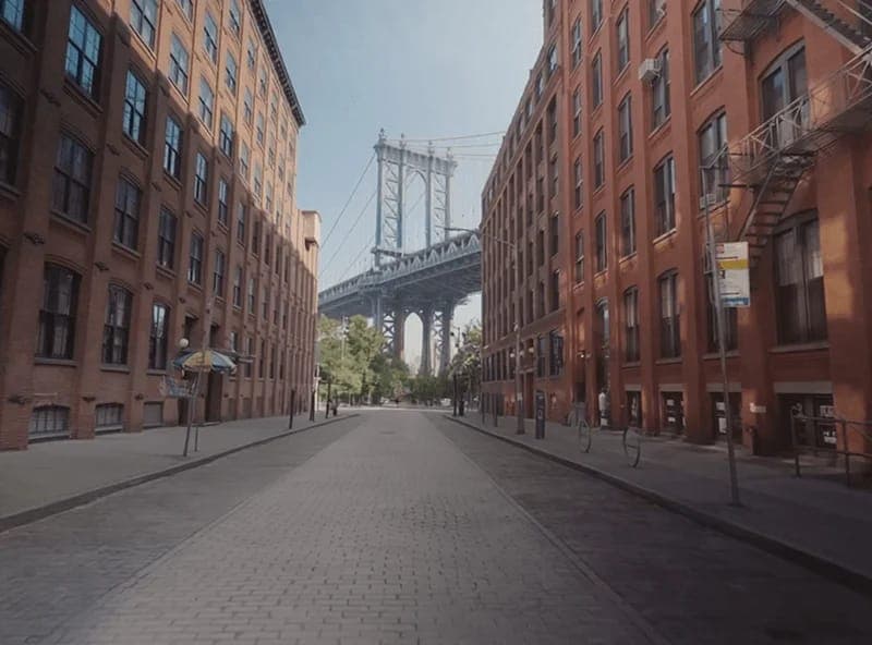 The image captures a view of the Manhattan Bridge, a prominent landmark in New York City. The bridge, painted in a striking shade of blue, stretches across the frame, its two towering pillars reaching towards the sky. The perspective is from a street, with the bridge appearing to recede into the distance. The street is