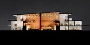 Night exterior of a glass-fronted restaurant or bar with warmly lit interior, diners at tables, and bottles on shelves. No visible text.