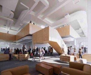Interior lobby with wooden stair volumes, white ceilings, and a crowd of people walking and sitting on light-colored seating. No legible text is visible.