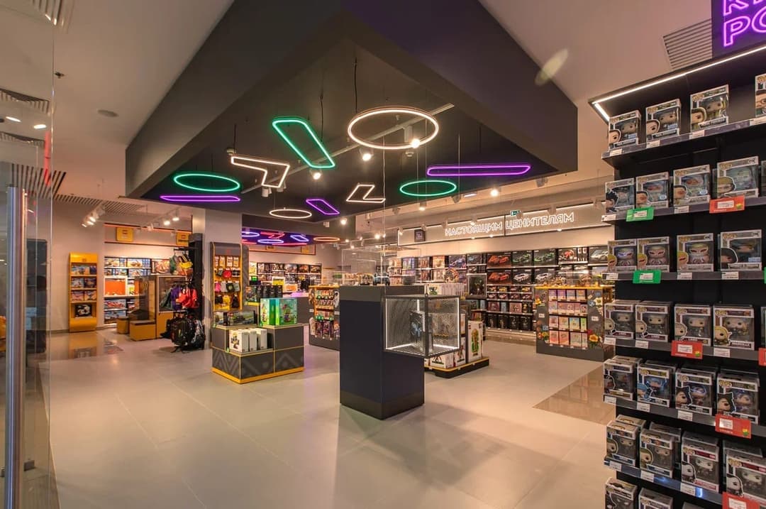 The image depicts a vibrant and colorful toy store. The store's ceiling is adorned with neon lights in shades of green, purple, and pink, creating a lively atmosphere. The store is filled with a variety of toys, including Funko Pop! figures, action figures, and collectibles, displayed on shelves and in glass cases. The