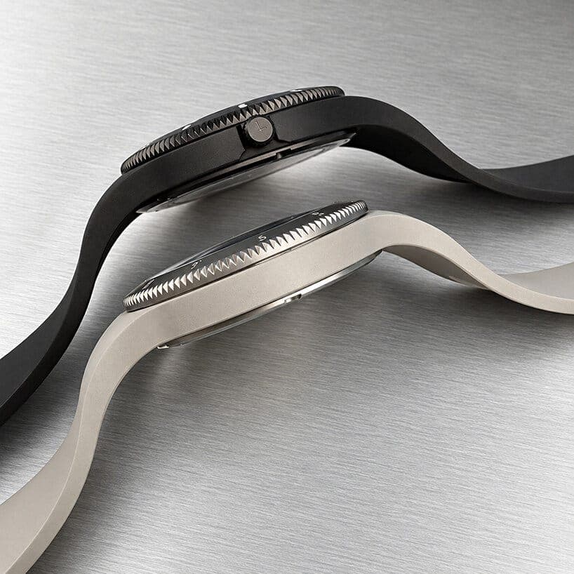 Two Lebond Norman Foster watches with rubber straps, one black and one sand-colored, lie side by side on brushed steel. Their knurled bezels are shown in profile.