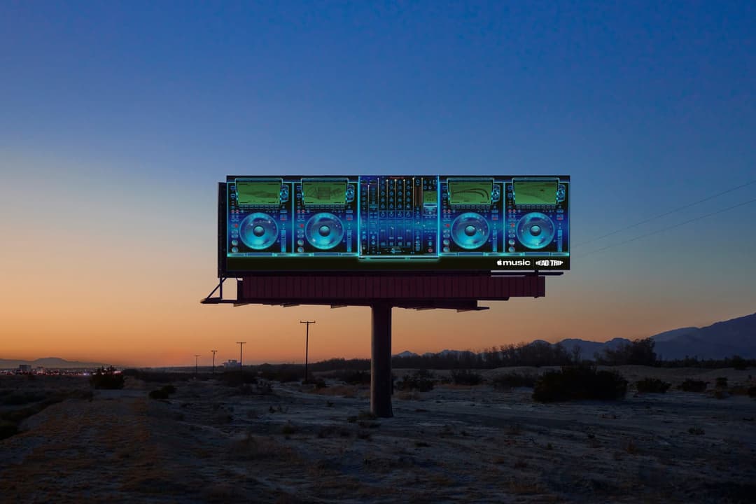 A billboard in a desert landscape at dusk displays illustrated DJ turntables and a mixer in glowing blue. The bottom corner shows the Apple Music logo and a second stylized logo that is only partly legible.