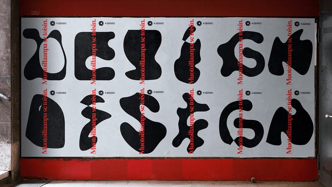 The image shows a vibrant red wall with a white poster affixed to it. The poster features a collection of black, abstract shapes and letters, including the word "DESIGN" in a stylized font. The letters and shapes are arranged in a grid-like pattern, with each element positioned at the top or bottom of the grid. The pos