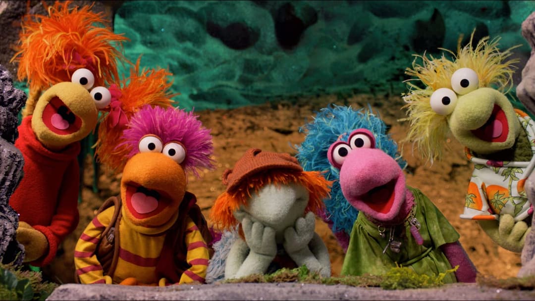 The image shows five animated puppets, likely from the Muppet show, gathered together in a scene that appears to be set in a cave or underwater environment. The puppets are positioned in a loose formation, with the largest on the left and the smallest on the right. The puppets are wearing colorful clothing, including a
