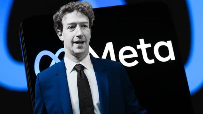 The image shows a man in a blue suit and black tie standing in front of a black smartphone. The smartphone displays the white text "Meta" in a stylized font. The man has curly hair and is looking towards the left side of the image. The background is a dark blue with a lighter blue circular design.