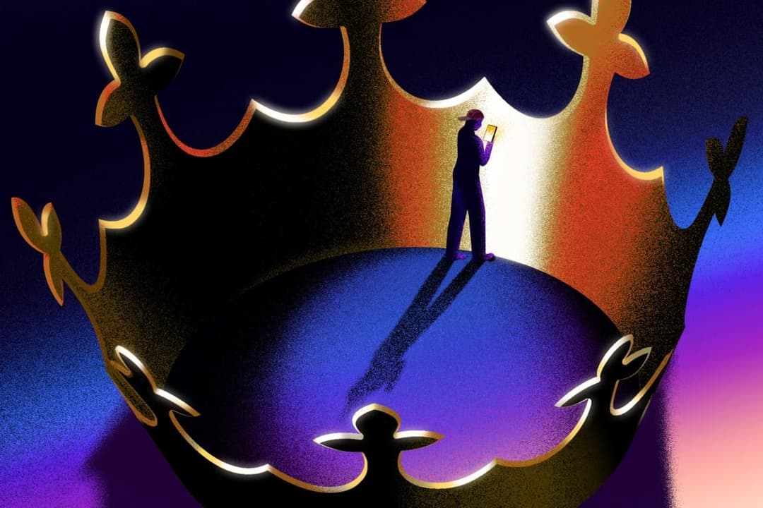 The image depicts a solitary figure standing on a large, ornate crown. The figure is wearing a dark blue or purple outfit and is holding a small, light-colored object, possibly a phone or tablet. The crown, a striking contrast of gold and black, is positioned centrally in the image and features intricate, stylized desi