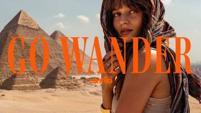 A woman with a bandana-style scarf stands before the Egyptian pyramids, with orange serif text reading "GO WANDER" and the Contiki logo across the image.