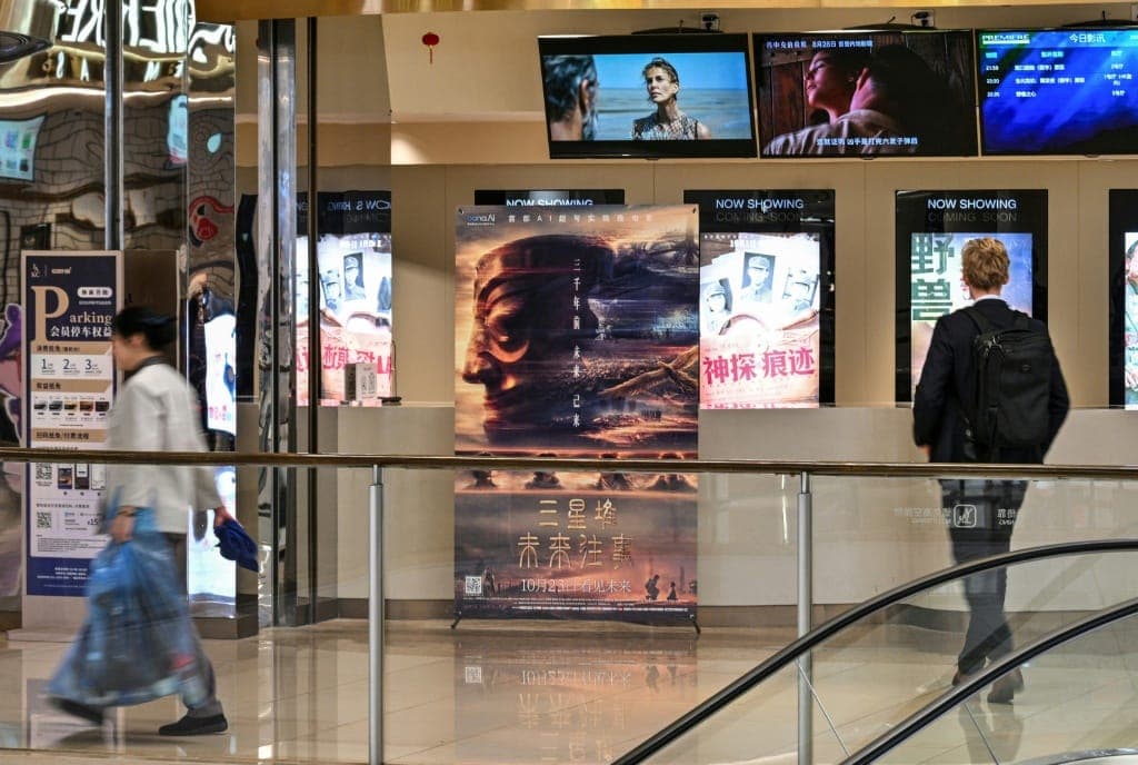 The image captures a scene in a shopping mall, likely in China. The central focus is a large movie poster for "The King's Speech" displayed on a wall. The poster features a large, stylized face and the title in English and Chinese. The poster is situated in a brightly lit area of the mall, with a glass railing separati