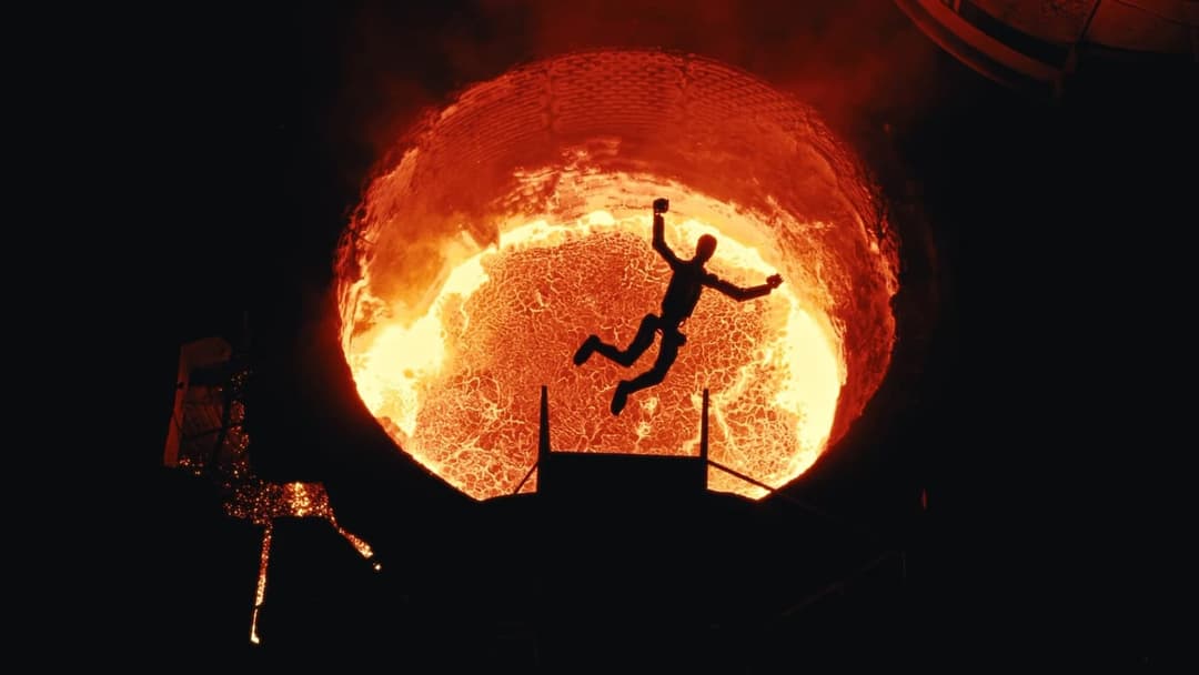 The image depicts a large, circular furnace with a bright orange glow, likely from burning coal or other fuel. A person is seen falling into the furnace, their silhouette stark against the fiery backdrop. The furnace is situated in a dark, industrial setting, with a portion of a structure or building visible in the bac
