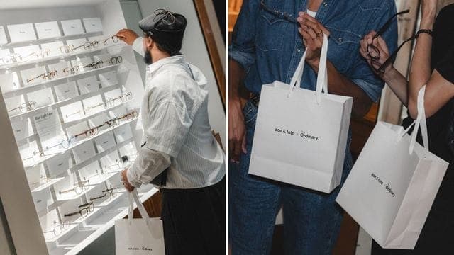 The image shows a man in a white shirt and black pants standing in front of a white display case filled with eyeglasses. He is holding a white shopping bag with the text "acme klass" and "Eyewear" printed on it. The display case is filled with a variety of eyeglasses, each with a unique design and color. The man is wea