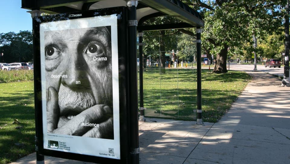 The image shows a black and white poster affixed to a black metal pole on a sidewalk. The poster features a close-up of a person's face with a surprised expression, and the text "Drama deserves an audience" is prominently displayed. The poster also includes the logos for the "Chicago Film Festival" and the "80s Cinema"