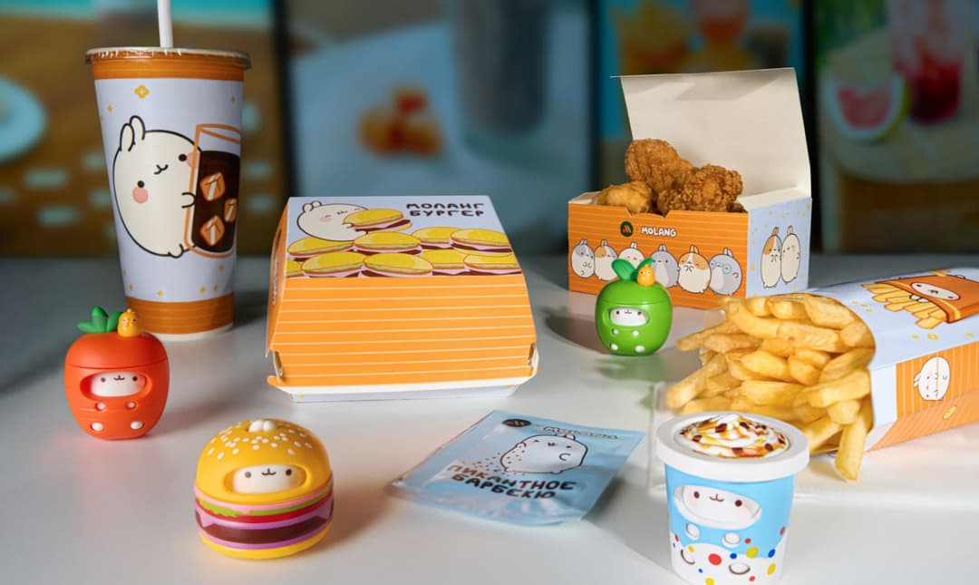 The image shows a collection of anime-themed food and drink items arranged on a white table. On the left side, there is a white cup with a cartoon rabbit holding a drink, a white box with a cartoon rabbit holding a sandwich, and a white box with a cartoon rabbit holding a sandwich. On the right side, there is a white b