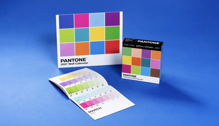 The image presents a collection of Pantone's wall calendar for the year 2027. The largest calendar is a square design with a vibrant color palette of pink, blue, green, yellow, and orange. It is placed on a blue background. Next to it is a smaller booklet with a color palette of pastel shades, including pink, blue, gre