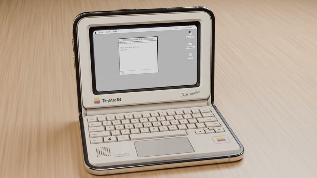The image shows a vintage Apple MiniMac 84 laptop with a beige or cream-colored exterior. The laptop is open, displaying a desktop screen with a gray background and a white text box containing a message. The message reads, "A little room for you. Make yourself at home. Hello, friend." The laptop has a black keyboard an