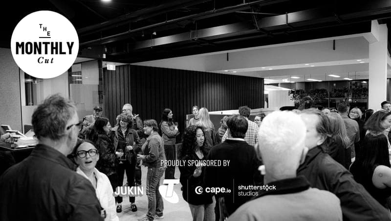 The image captures a lively gathering of people in a modern office space. The room features a black and white color scheme, with a black wall and ceiling, and a large window on the left side. The people are engaged in conversation, some standing and others seated, creating a dynamic atmosphere. The room is well-lit, wi