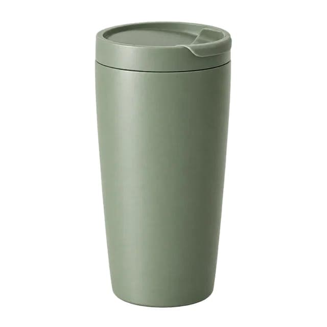 The image shows a single, light green travel mug with a lid. The mug has a slightly curved shape and a small indentation on the top for a handle. It is positioned centrally against a black background, which highlights its vibrant color and design. The mug appears to be made of a matte material, and the lid is closed.