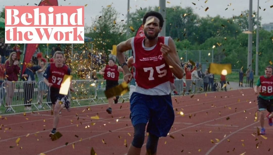 The image captures a dynamic scene from a track race, with a runner in a red jersey with the number 75 prominently featured in the foreground. The runner is in the midst of a powerful stride, his body leaning forward with determination. The runner is surrounded by a blur of other runners, all wearing red jerseys, creat