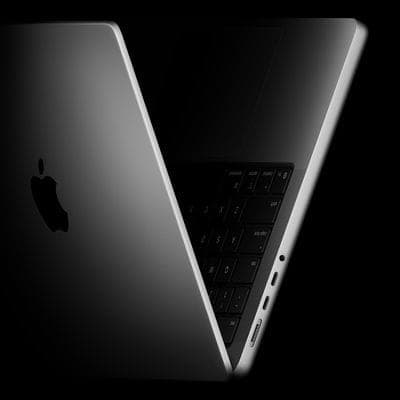 The image shows a sleek, silver Apple MacBook laptop with a black keyboard and trackpad, positioned at an angle against a black background. The laptop is open, revealing the keyboard and trackpad, and is angled slightly to the right. The Apple logo is prominently displayed on the left side of the laptop. The laptop's s