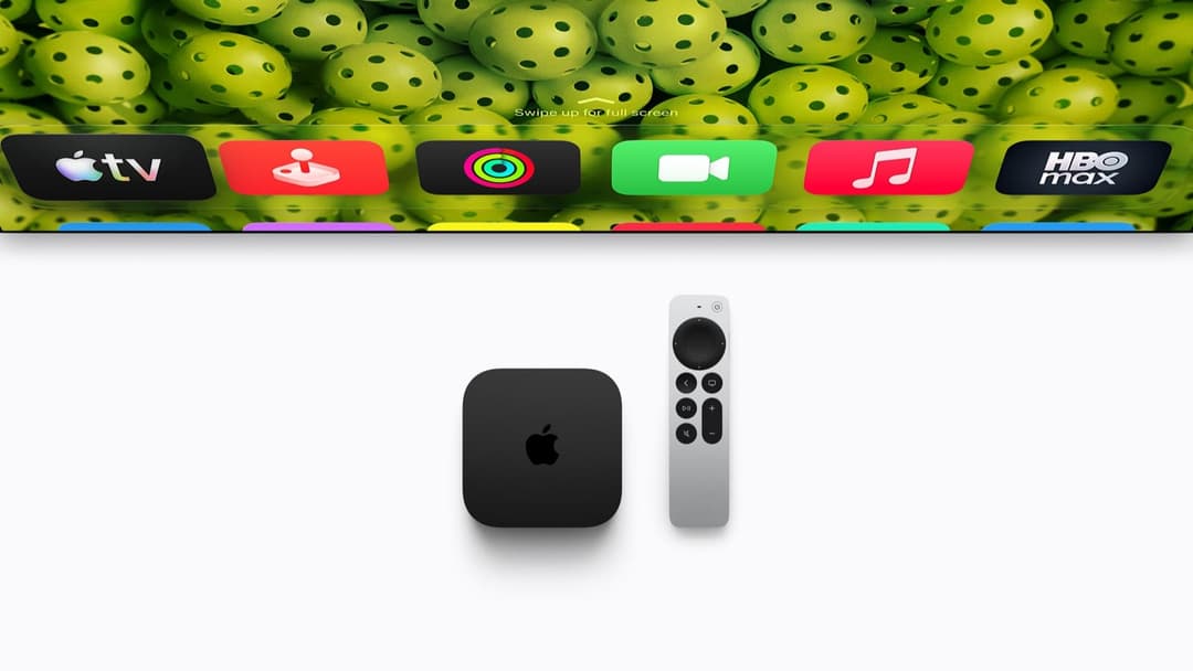The image presents a scene of a smart TV setup. At the center is a black Apple TV, with a white remote control placed to its right. The TV is positioned on a white surface, with a background of a vibrant display of green ping pong balls. The background also features a row of app icons, including Apple TV, a red and whi