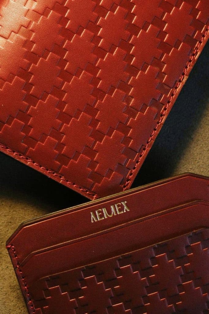 The image shows a close-up view of a brown leather wallet with a distinctive herringbone pattern. The wallet is folded in half, revealing its embossed design. The embossed pattern is a repeating geometric design, creating a visually appealing texture. The wallet is made of leather and has a slightly textured surface. T