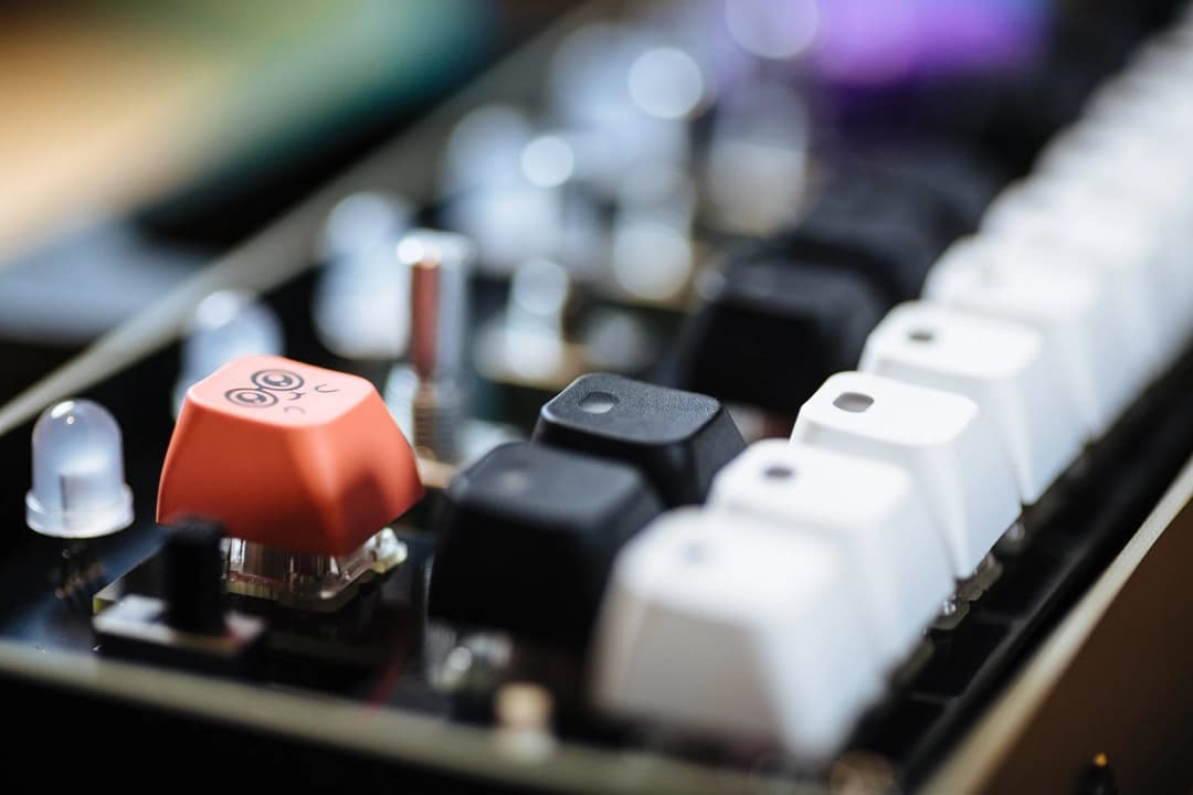 The image shows a close-up view of a circuit board, likely part of a computer keyboard or similar electronic device. The circuit board is black and features a row of white keys, with a row of black keys in the middle. The keys are arranged in a standard QWERTY layout. A row of small, round, white LED lights are visible