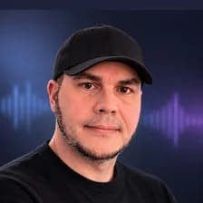 The image shows a man with a serious expression, wearing a black baseball cap and a black t-shirt. He has short, dark hair and a short, neatly trimmed beard. The background is a dark blue with a faint purple/lavender audio wave pattern.