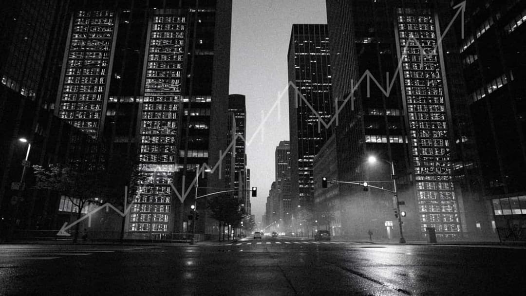 This black and white photograph captures a city street at night, with tall buildings lining both sides of the street. The buildings are illuminated by the glow of their windows, creating a stark contrast against the dark sky. The street is relatively empty, with a few cars visible in the distance. The street appears we