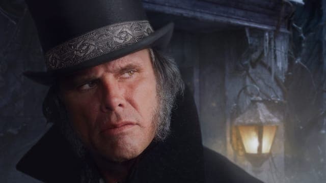 The image shows a man with a stern expression, wearing a black top hat with a silver band and a black coat. He has a gray beard and mustache and is looking off to the side with a serious expression. The background is dark and out of focus, with a partially visible, possibly stone, structure and a lit lantern visible. T